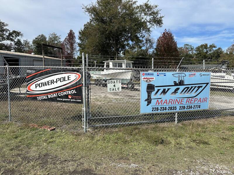 Fenced boat yard behind the light-blue In & Out Marine Repair sign, with shop buildings in back
